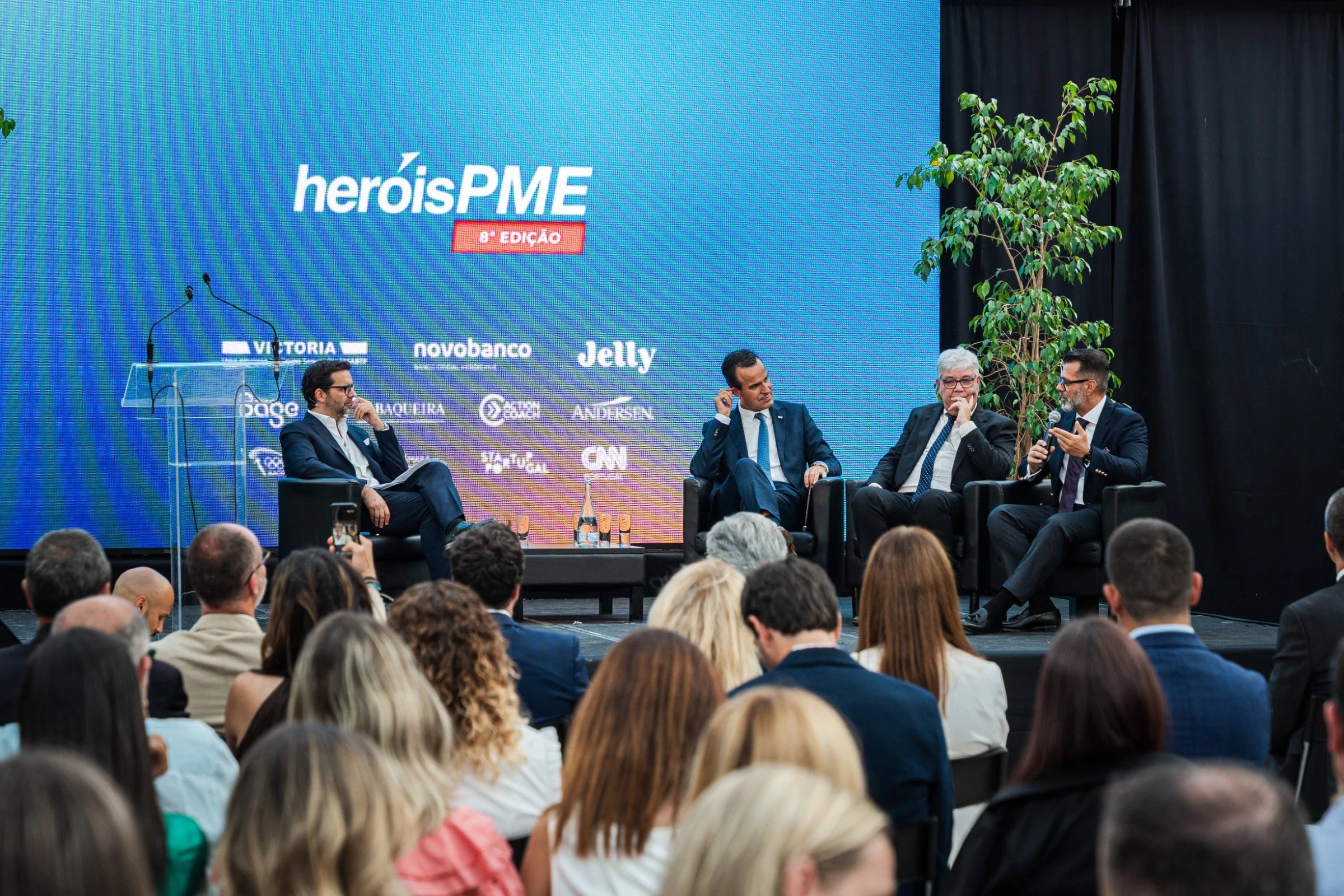 Quatro oradores em painel num palco, diante de ecrã com "heróisPME 6ª Edição" e logótipos incluindo "Jelly"