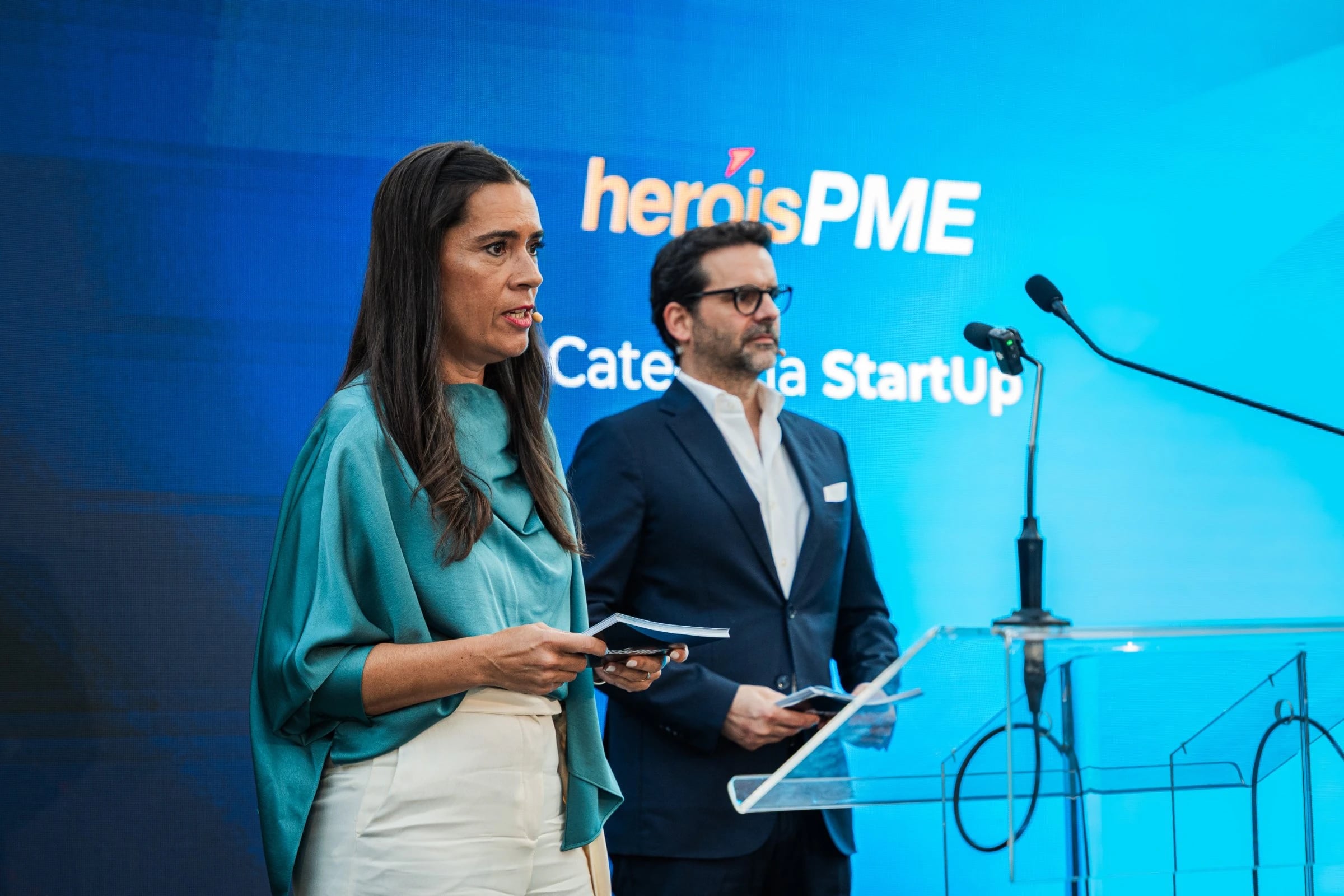 Mulher e homem junto a púlpito perante ecrã azul com "heróisPME" e "Categoria StartUp"