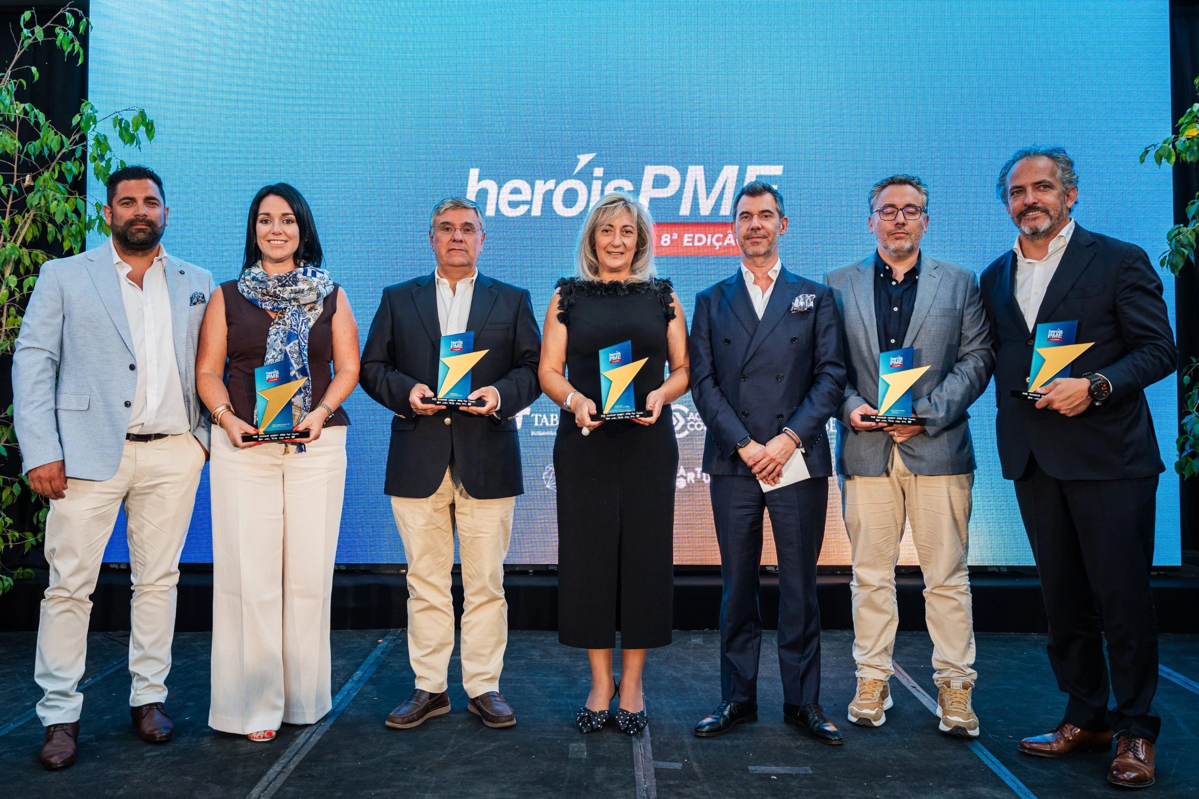 Sete pessoas em palco, quatro com troféus, diante de ecrã com "heróisPME 8ª Edição"