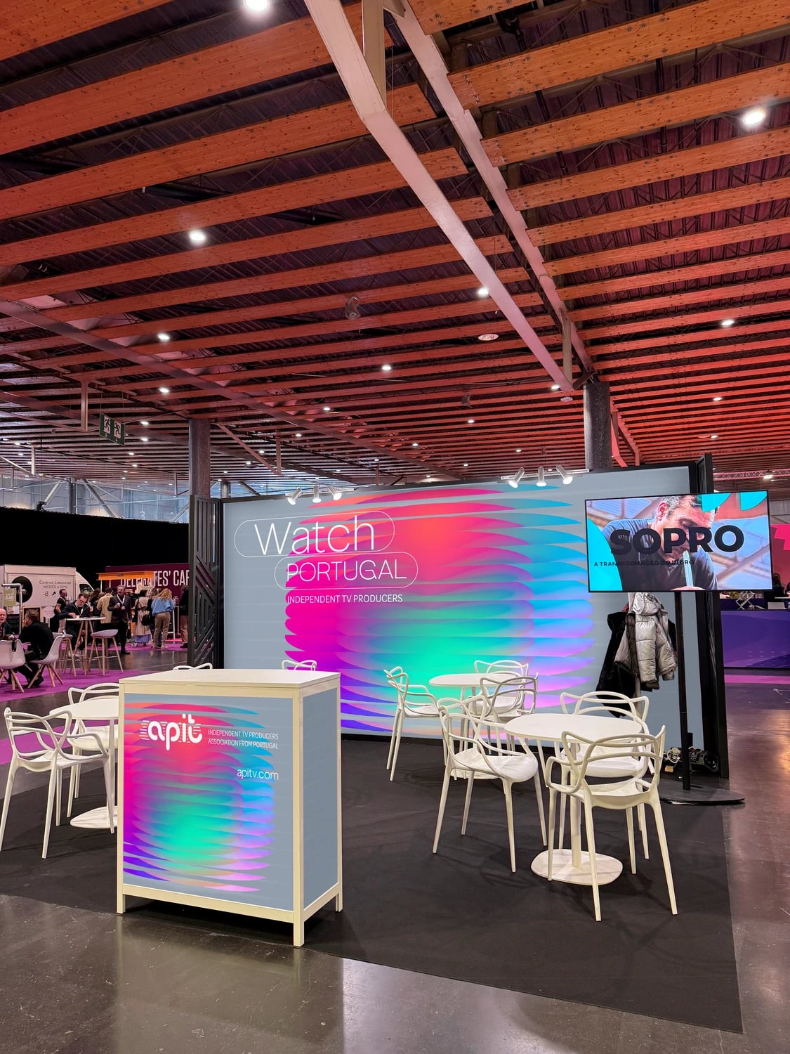 Stand de feira com painel "Watch Portugal Independent TV Producers", balcão "apit" e mesas e cadeiras brancas