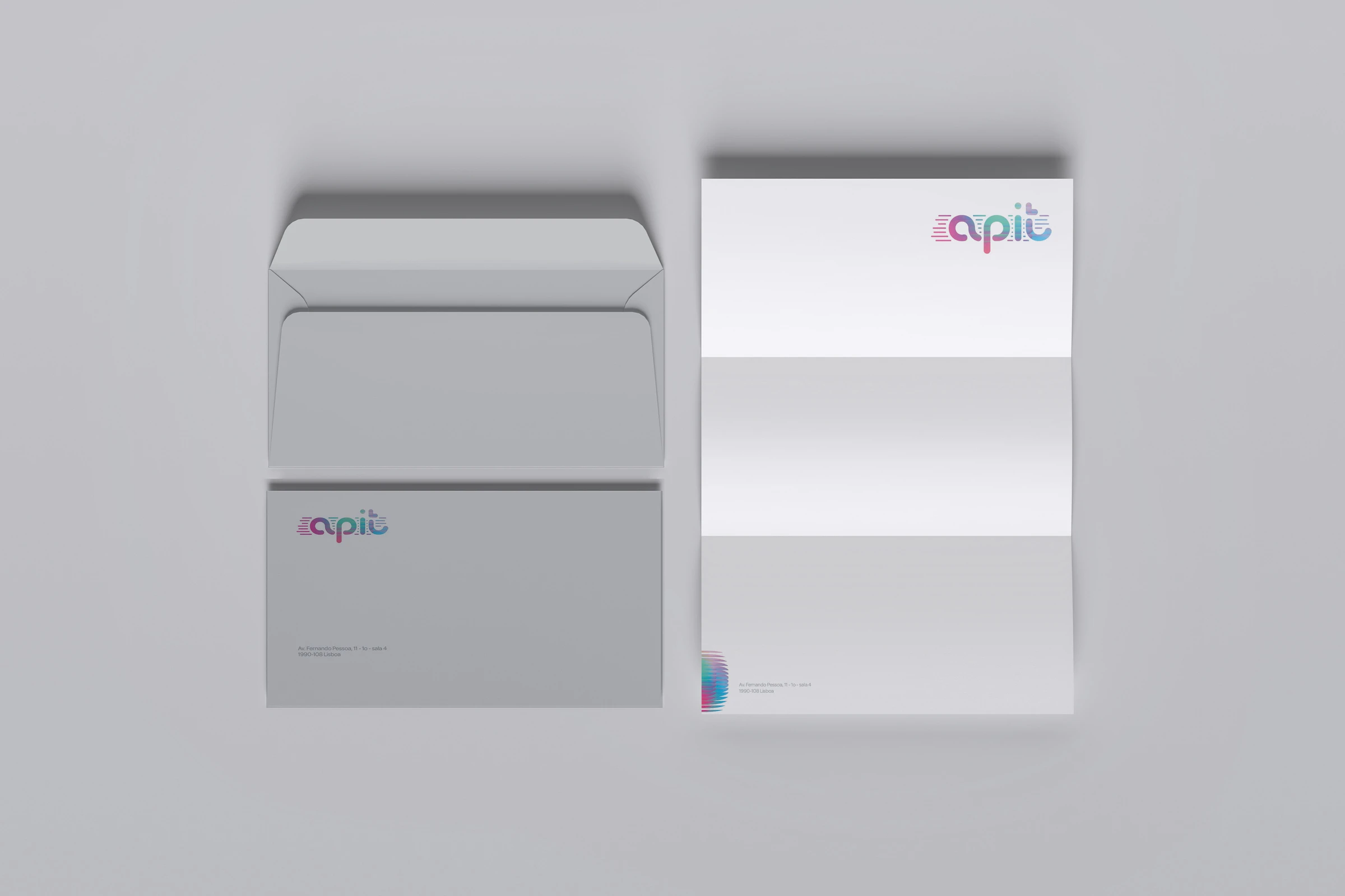 Envelopes e papel de carta dobrado cinza-claros com o logótipo "apit" em gradiente rosa e azul