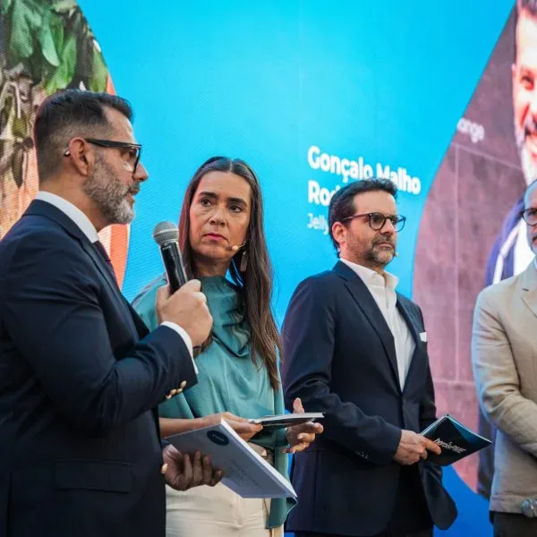 Quatro oradores em palco num evento, com ecrã a exibir o nome Gonçalo Malho Rodrigues da Jelly, segurando microfone e brochuras