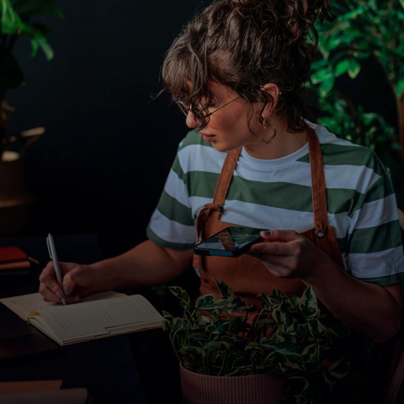 Senhora a escrever num caderno rodeada de flores